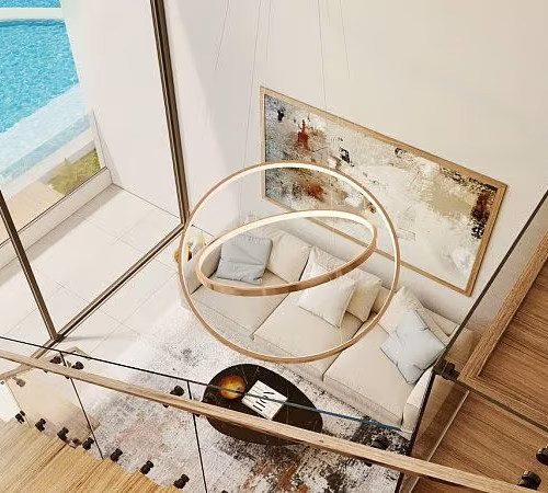 Luxurious living room with a modern chandelier, beige sofa, and abstract wall art, viewed from an upper-level balcony. Features floor-to-ceiling windows overlooking a private pool.